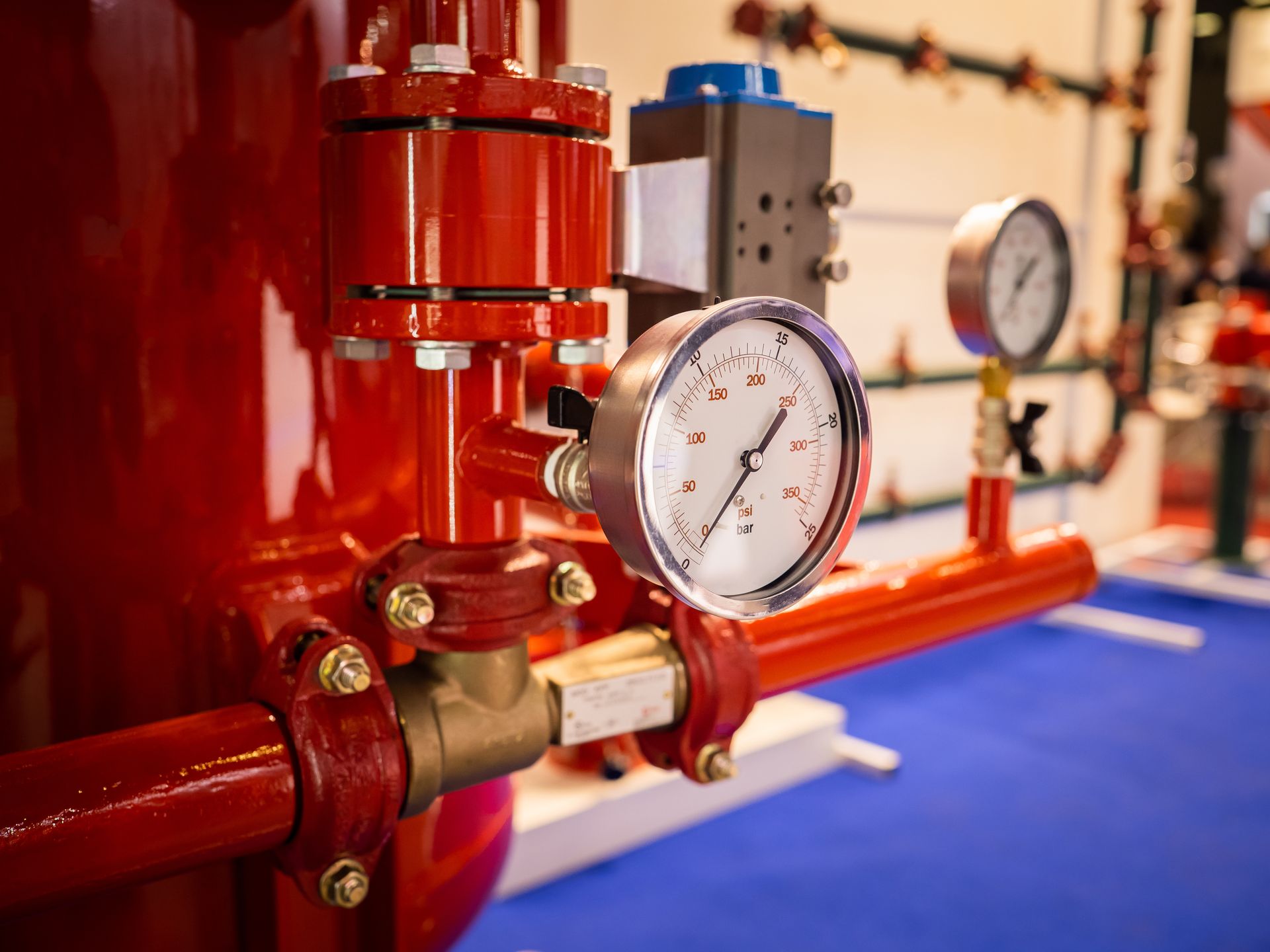 Red industrial pipes with pressure gauges and valves in a mechanical room