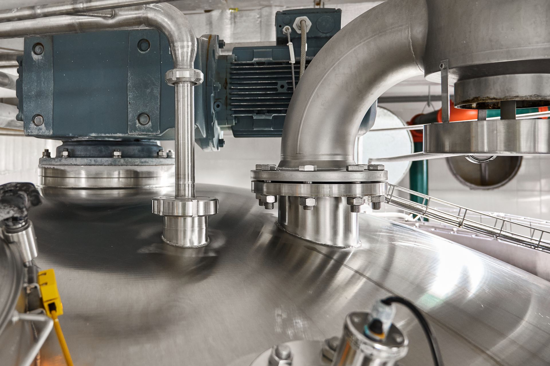 Close-up of stainless steel industrial piping, valves, and motor equipment in a processing tank area