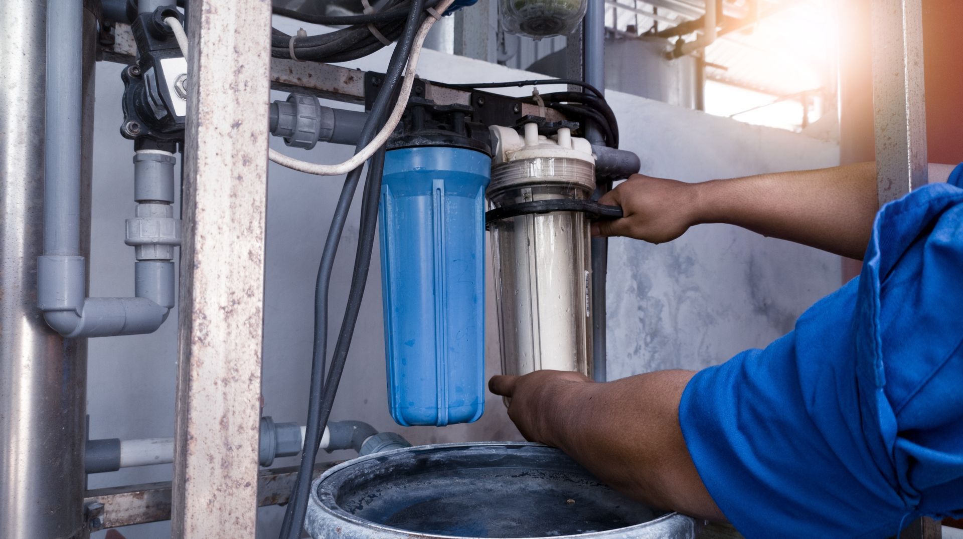Technician installing a blue water filter under a sink with exposed plumbing