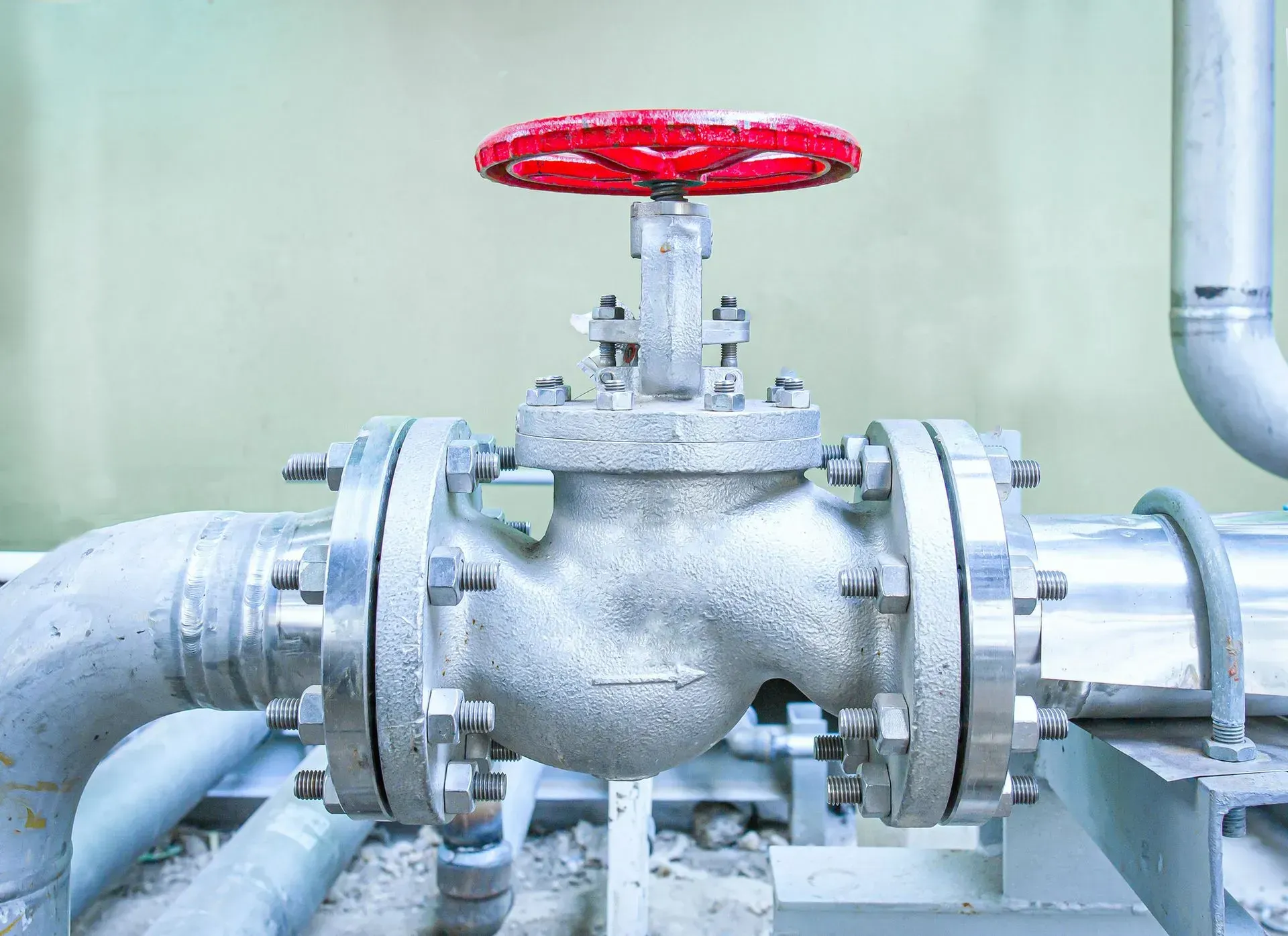 Industrial pipe valve with red handwheel on a large gray pipeline