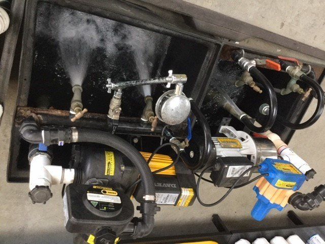 Engine compartment with hoses, pumps, and wiring mounted on a black panel.