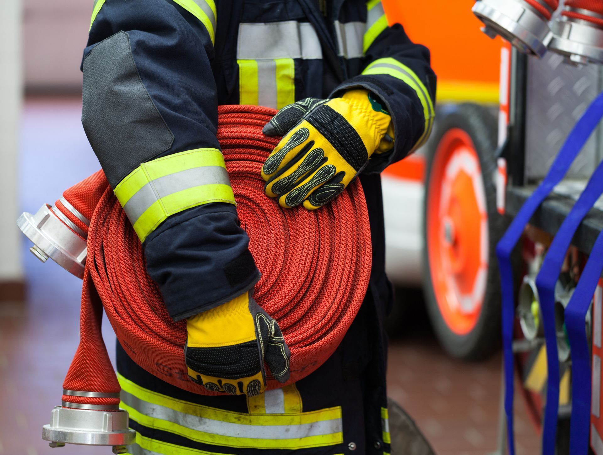Firefighter holding a coiled red hose in reflective gear beside a fire truck