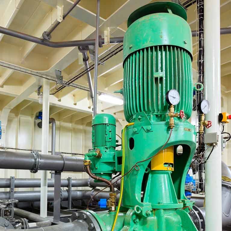 Green industrial pumps and pipes in a machinery room, with gauges and overhead piping.