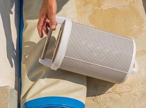 Hand holding a white cylindrical pool filter cartridge over a beige surface