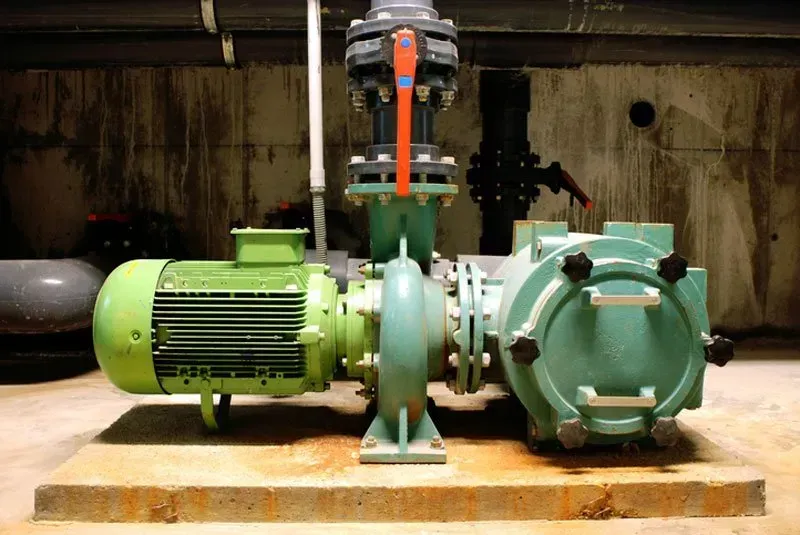 Green industrial motor and pump assembly mounted on a wooden base in a dim factory setting