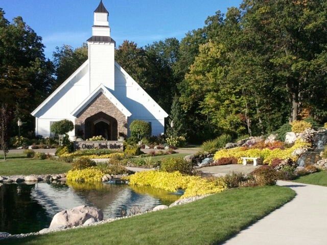 White church with stone facade by a pond with yellow plants and pathway.