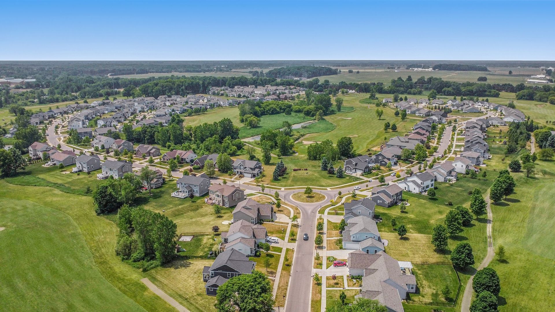 Aerial view of a suburban residential area with houses, streets, and green spaces under a blue sky.