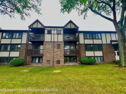 Brown brick and timber Tudor-style apartment building with balconies and green lawn.