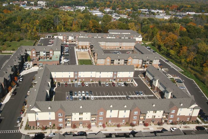 Aerial view of a large apartment complex with multiple buildings, parking, and surrounding trees.