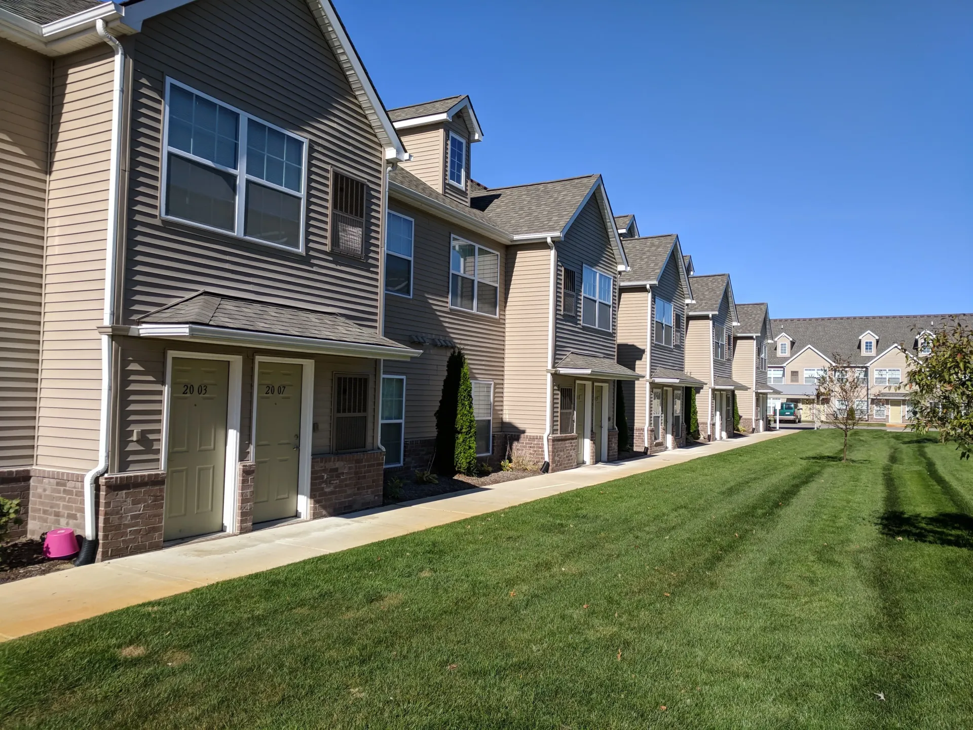 Row of tan and gray townhouses with green lawns and a blue sky.