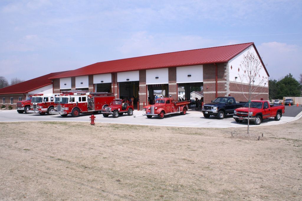 Fire station with red roof, open bays, and fire trucks parked outside.