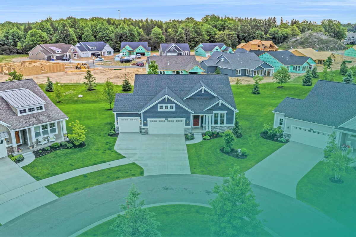 Aerial view of suburban homes with blue and gray siding, green lawns, and new construction in the background.