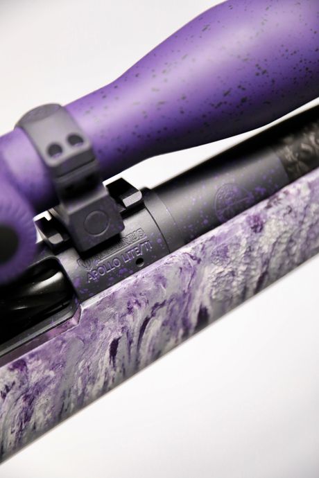 Close-up of a rifle with a purple scope, bolt, and stock with a marbled purple and white pattern.