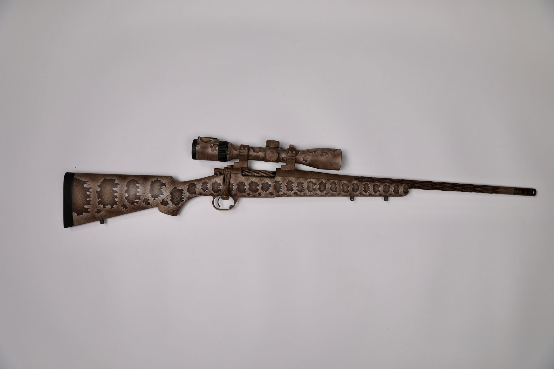 Rifle with scope, camouflage pattern on stock and optics, against a white background.