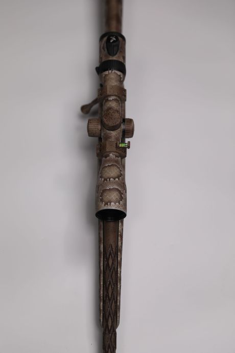 Close-up of a rifle scope mounted on a wooden rifle stock against a white background.