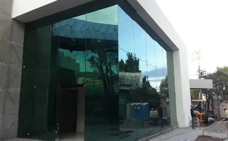 Entrada de edificio moderno con gran fachada de vidrio y marco blanco, con materiales de construcción cerca.