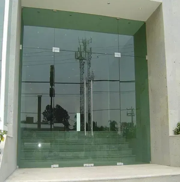 Entrada de cristal con puertas reflectantes, escalones detrás y estructura de hormigón.