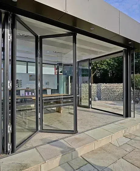 Entrada moderna de cristal con puertas abiertas y pasarela de piedra que conduce al interior.
