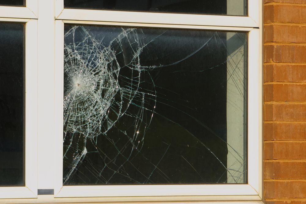 Cristal de ventana agrietado con vidrios rotos junto a una pared de ladrillos.