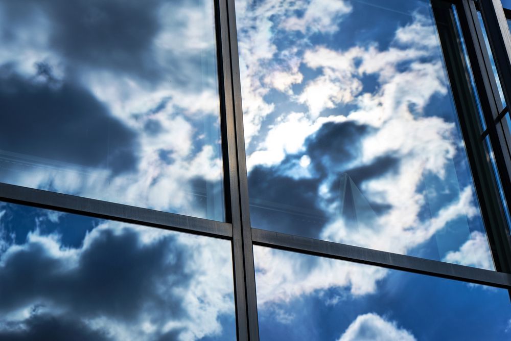 Reflejos del cielo azul y las nubes en la fachada de cristal de un edificio.