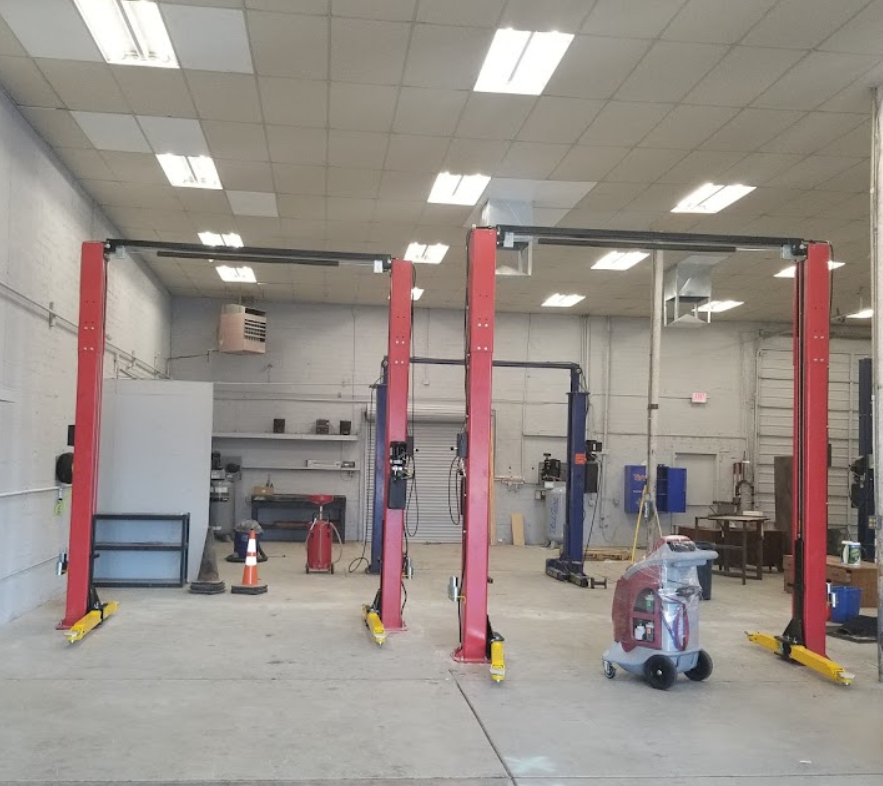 Garage interior with red car lifts, fluorescent lights, and a concrete floor. | Top Notch Autocare