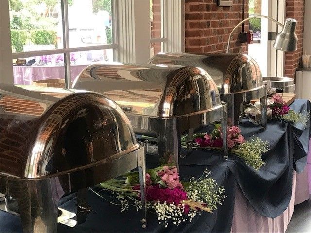 A buffet table with stainless steel containers and flowers on it.