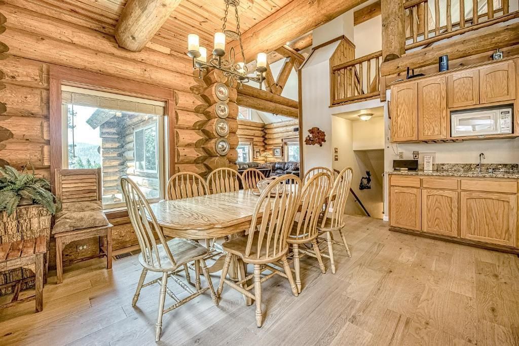 Rustic log cabin dining room with wooden table, chairs, chandelier, and kitchen cabinets