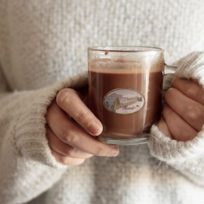 Hands holding a glass mug of hot chocolate, wearing a white sweater.