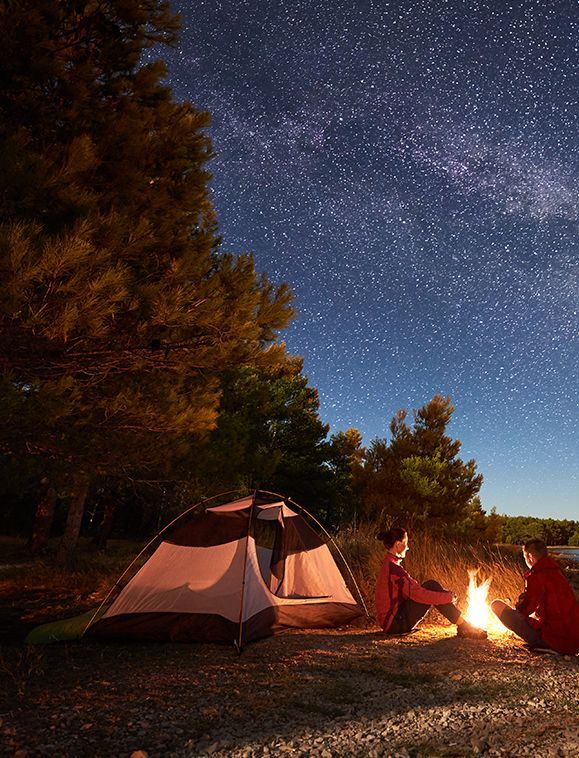 Campers by a campfire beneath a starry night sky near a tent.