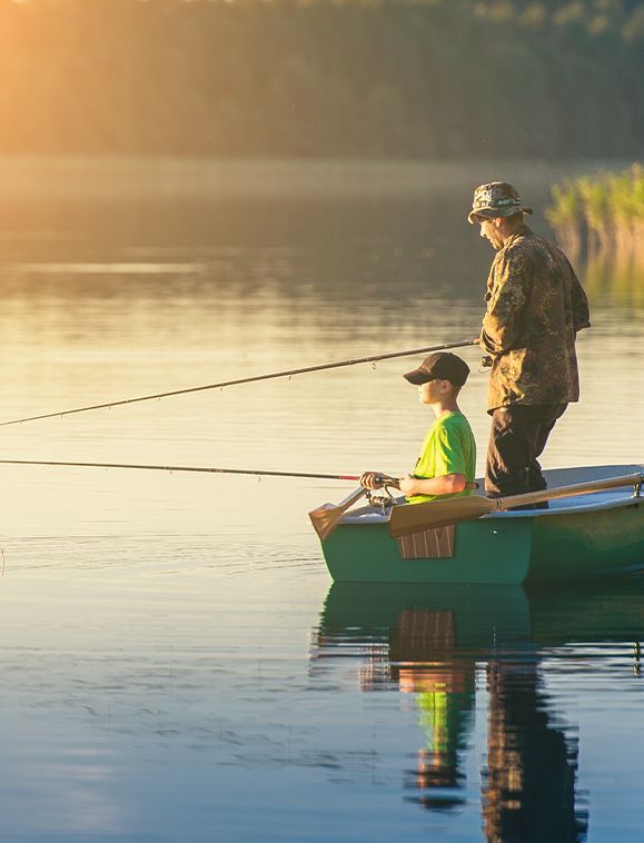 Man and boy fishing from a small boat on a calm lake at sunset.