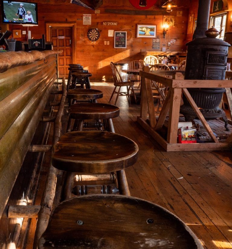 Rustic bar interior with wooden stools, a wood-burning stove, and a television.