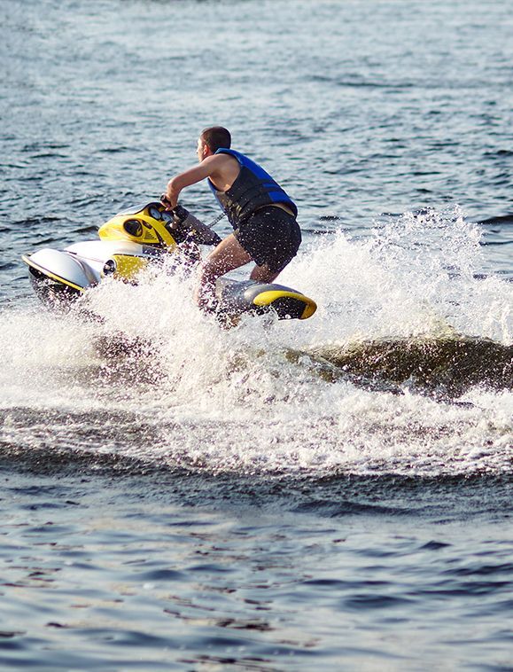 Person riding a jet ski, spraying water. Water is dark blue. Jet ski is white and yellow.