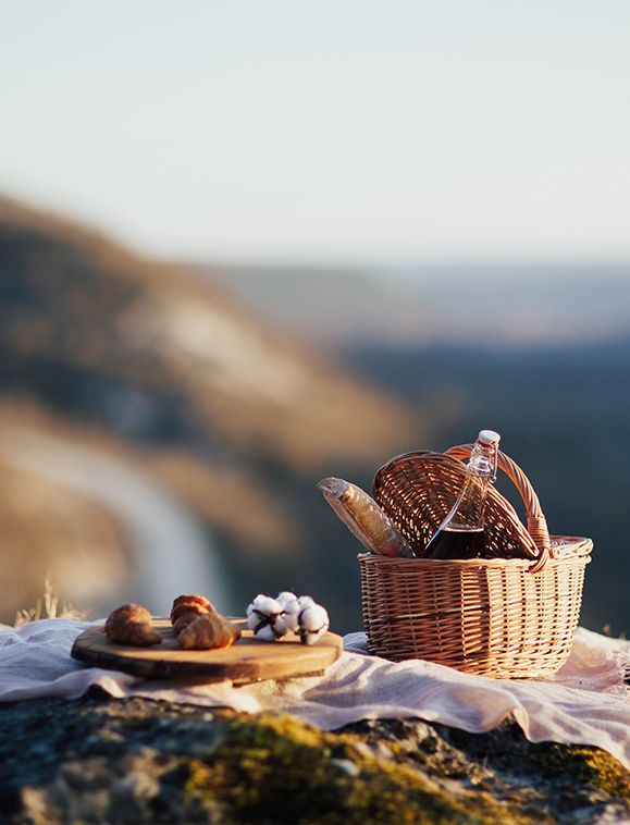 Picnic basket with food and drink on a cliff overlooking a scenic valley.