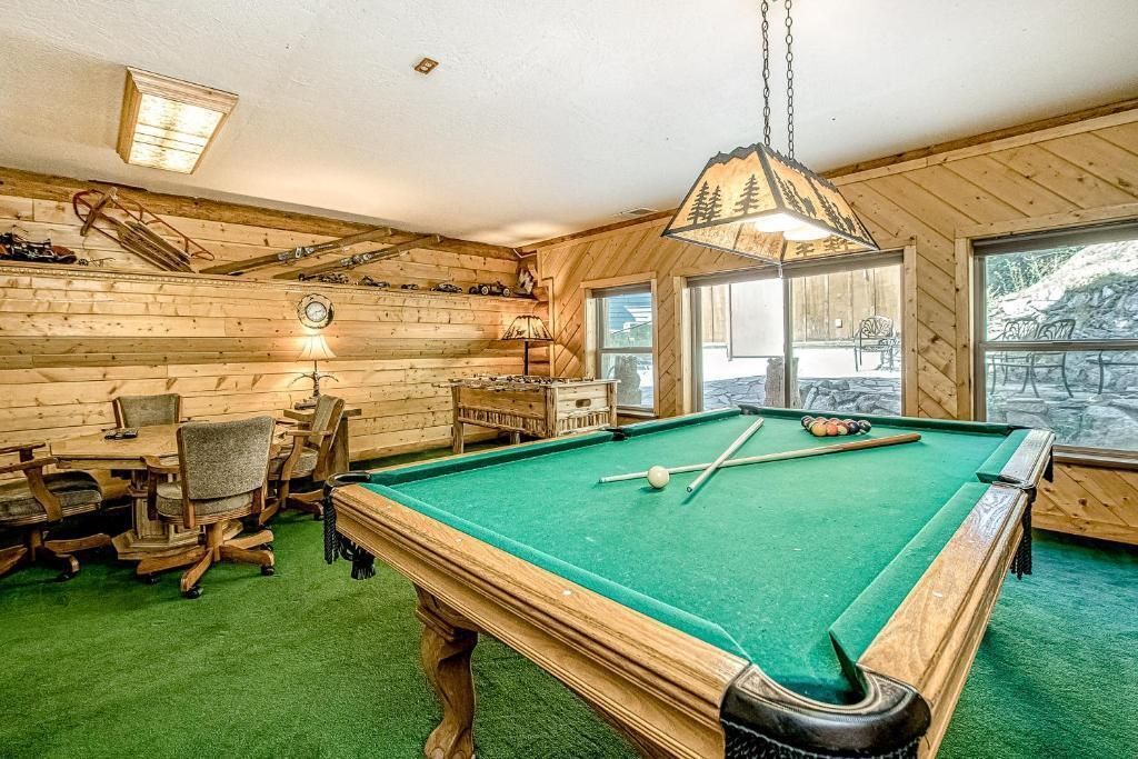 Rustic game room with a green pool table, wood-paneled walls, and large windows