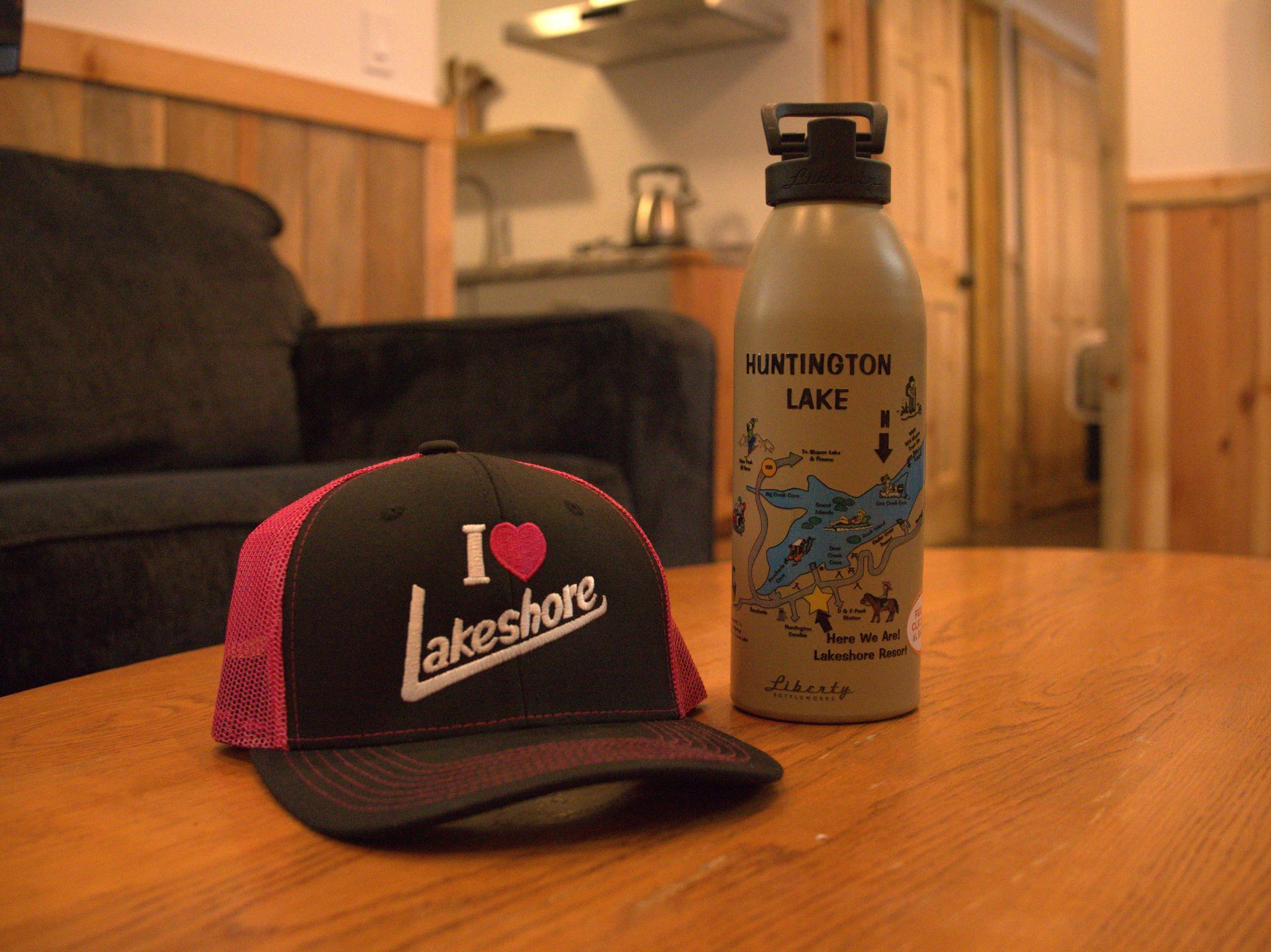 A black-and-pink cap on a wooden table beside a water bottle in a living room.