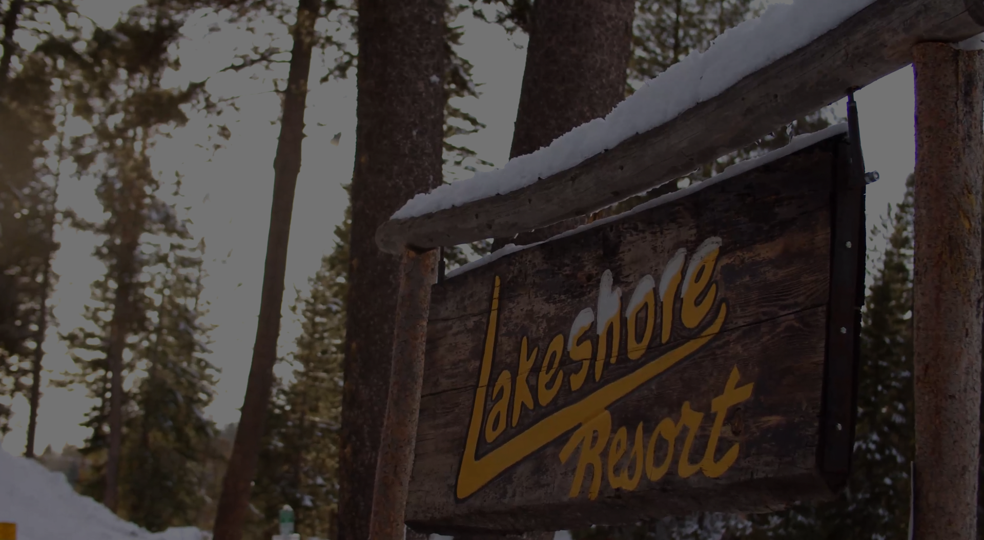 Lakeshore Resort wooden sign in a snowy forest.