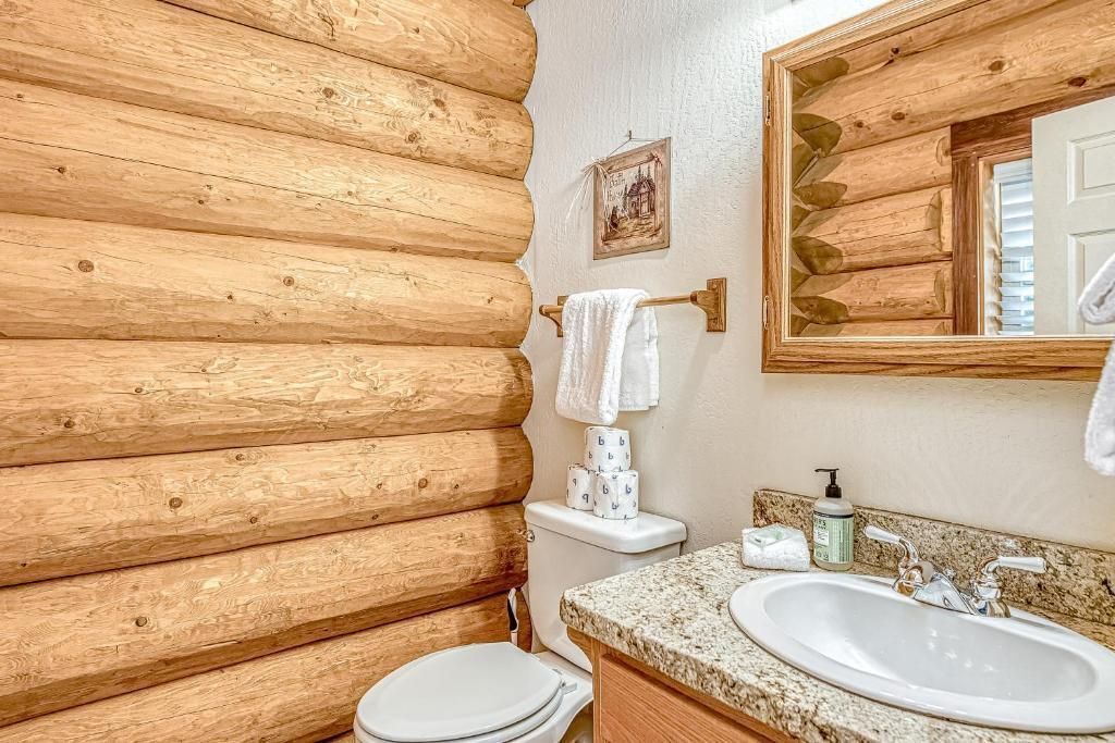 Small rustic bathroom with log walls, white sink, toilet, and a mirror above the vanity.