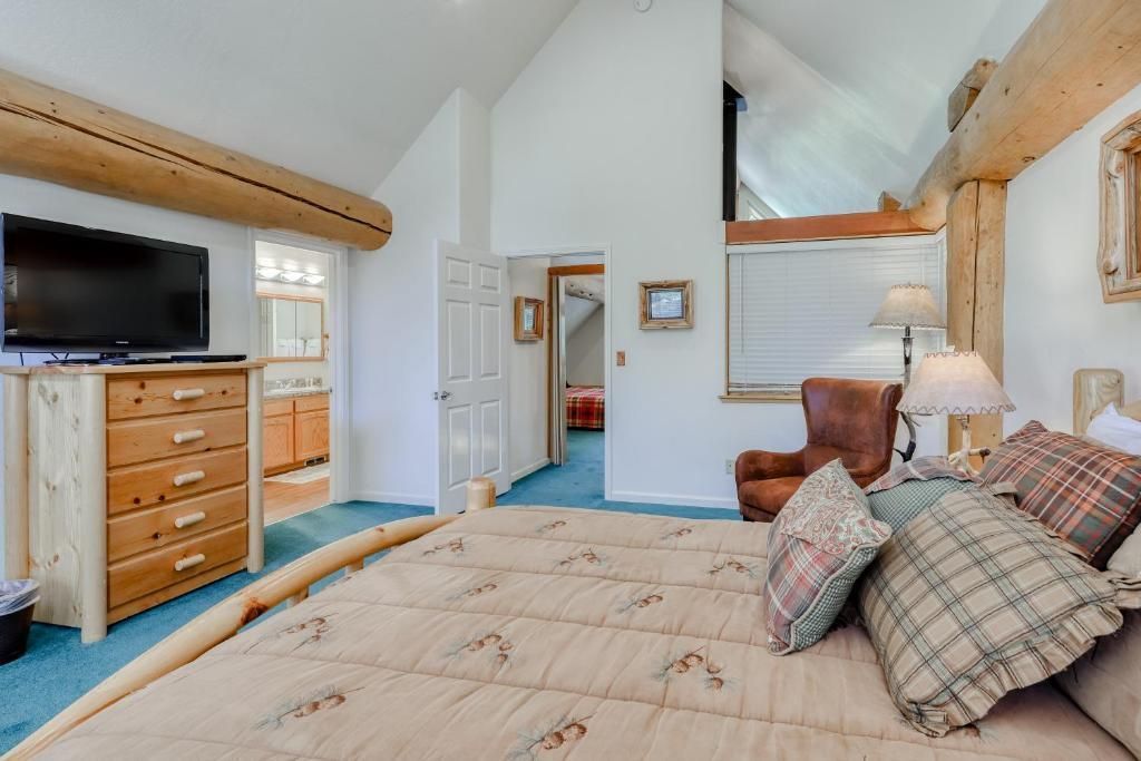 Bright bedroom with a wooden dresser, TV, bed with plaid pillows, and vaulted ceiling