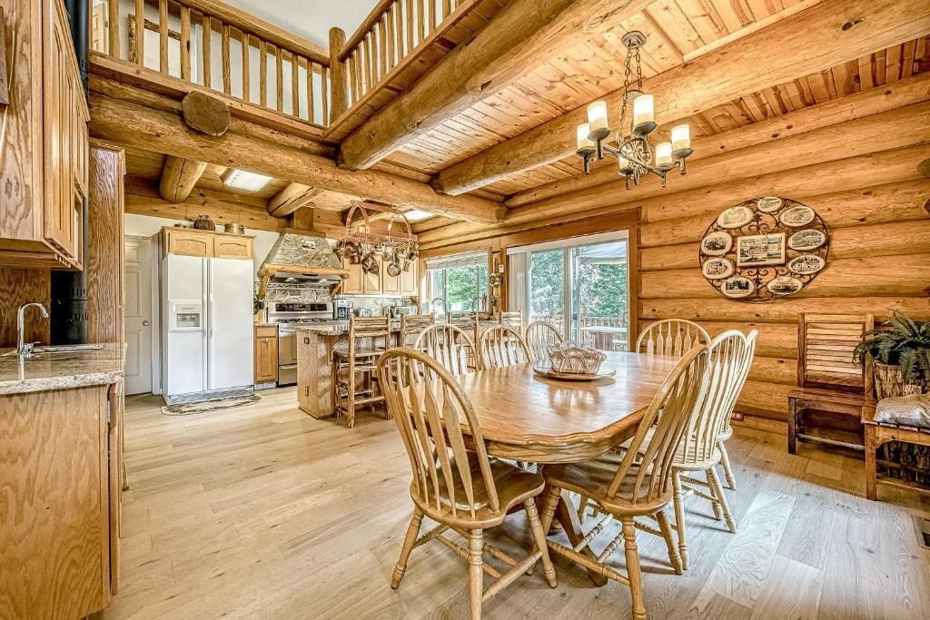 Rustic log cabin dining room with wooden table, chairs, chandelier, and large windows