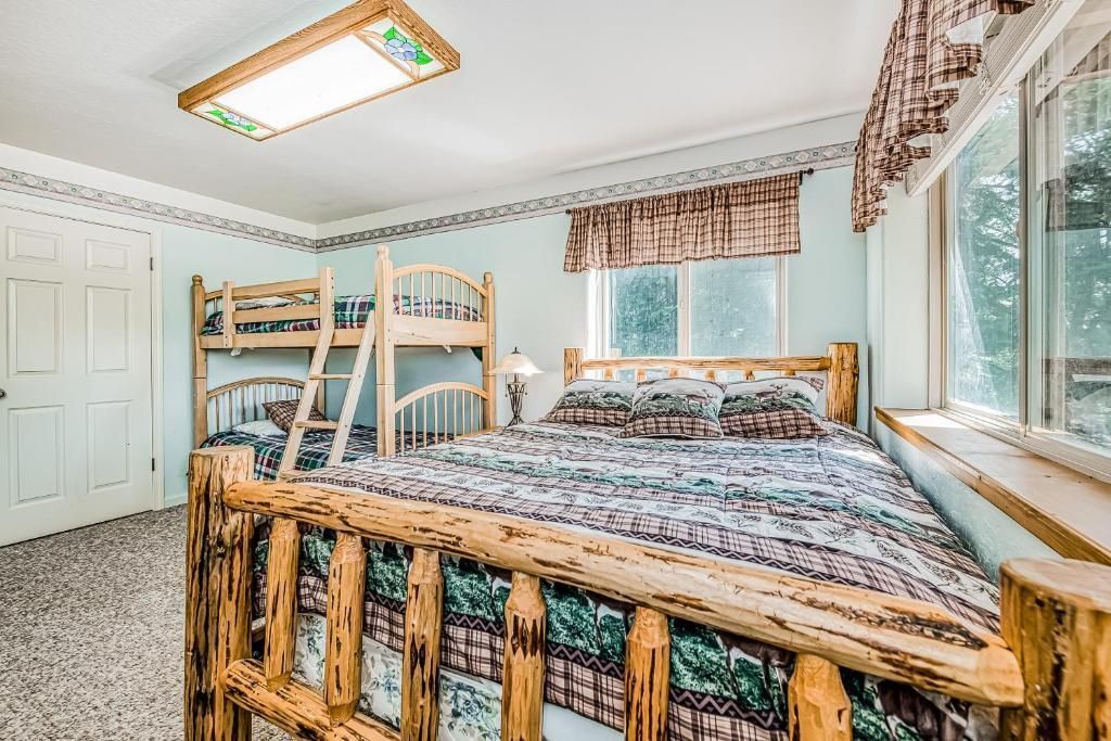 Bright bedroom with wooden bunk beds, a large bed, white walls, and windows with floral curtains.