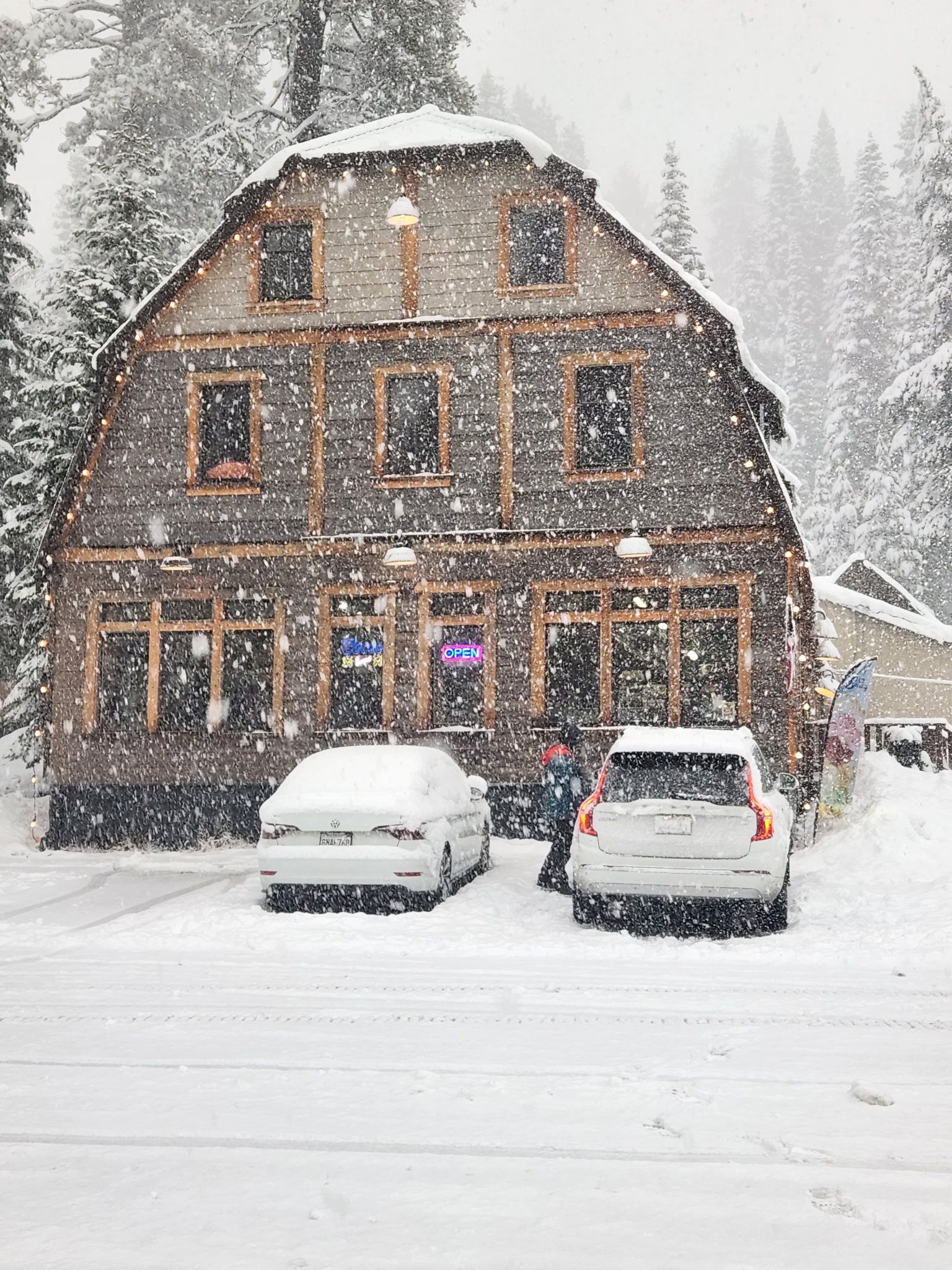 Snow-covered rustic house with two parked cars in a heavy snowfall