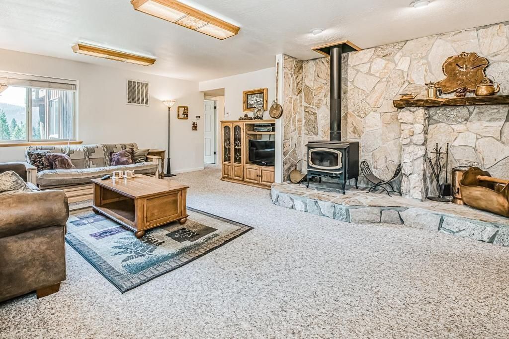 Spacious living room with stone fireplace, beige furniture, blue rug, and bright windows