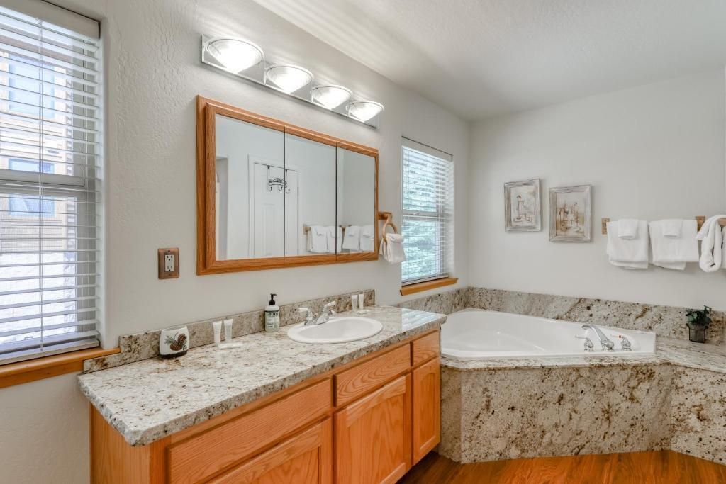 Bright bathroom with granite double vanity, wood cabinets, mirror lights, and a corner soaking tub.