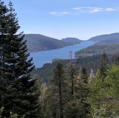 Lake surrounded by forested hills under a blue sky.