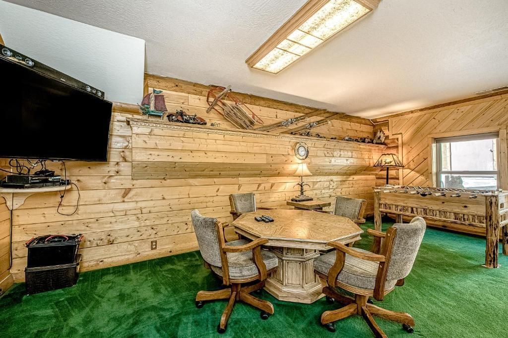 Wood-paneled room with round table, rolling chairs, green carpet, wall-mounted TV, and overhead fluorescent light
