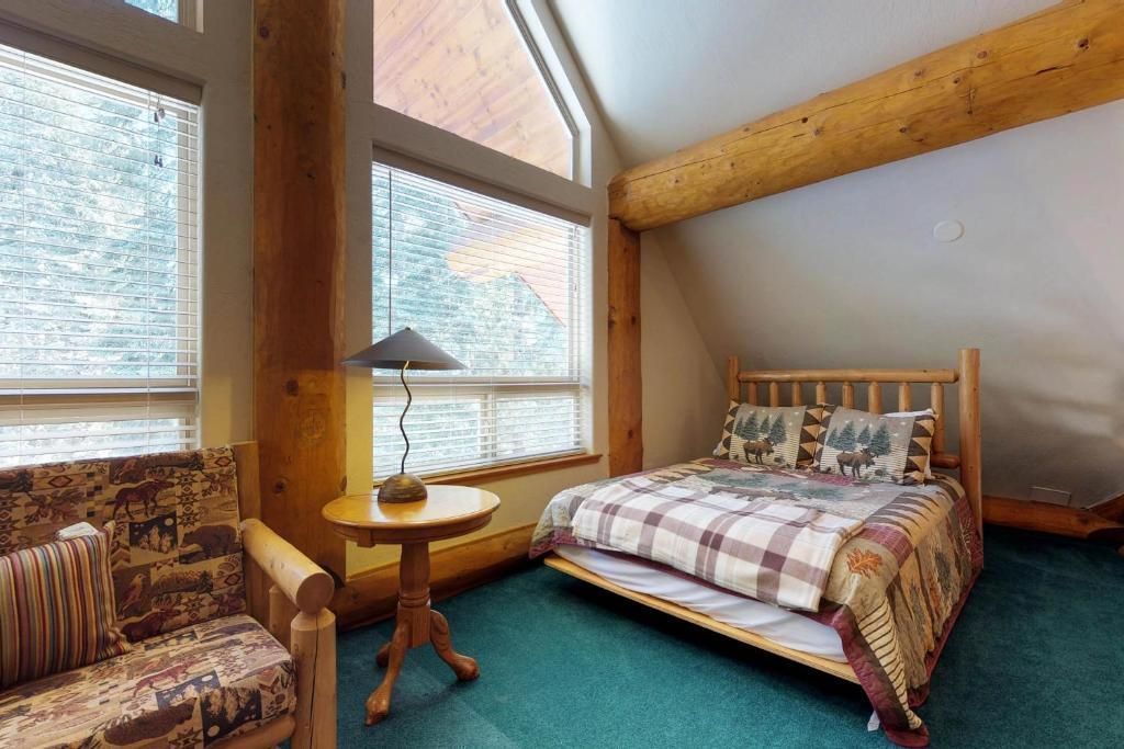 Cozy bedroom with large windows, wooden chair, round table, and bed with plaid bedding.