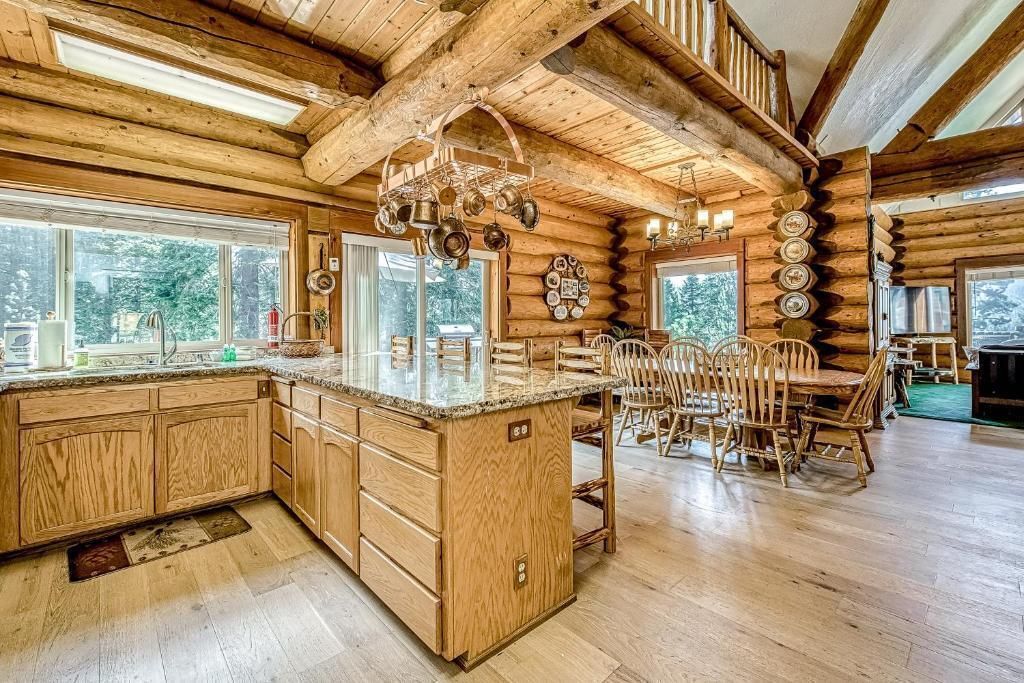 Rustic log cabin kitchen and dining area with wooden beams, large windows, and chandelier