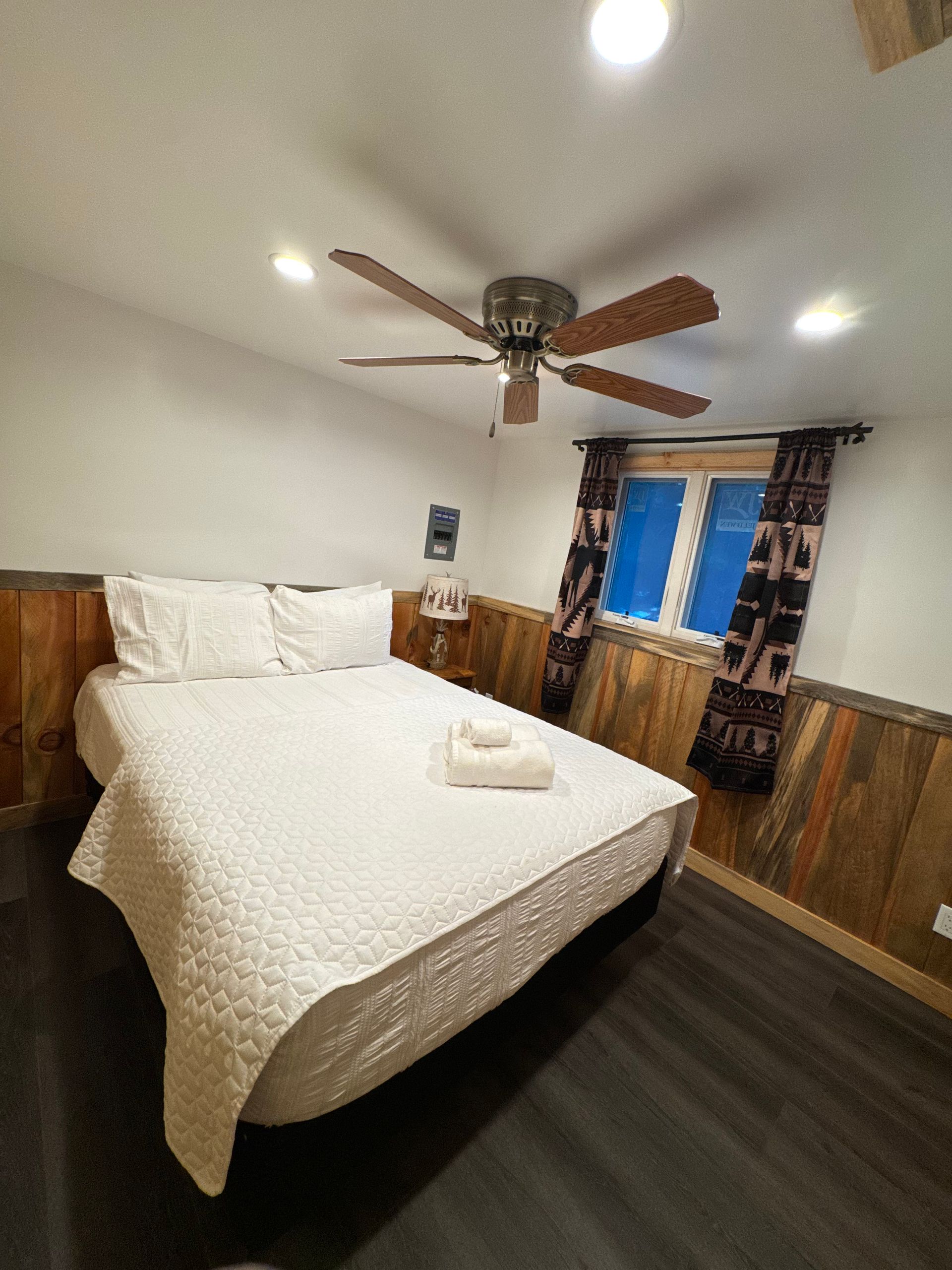 Bedroom with a bed, ceiling fan, wooden paneling, and a window with blue blinds.