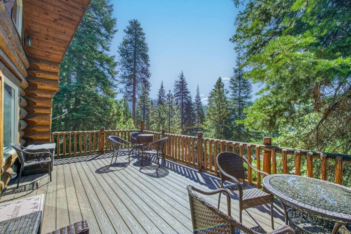 Wooden cabin deck with chairs and tables overlooking a sunny forested view