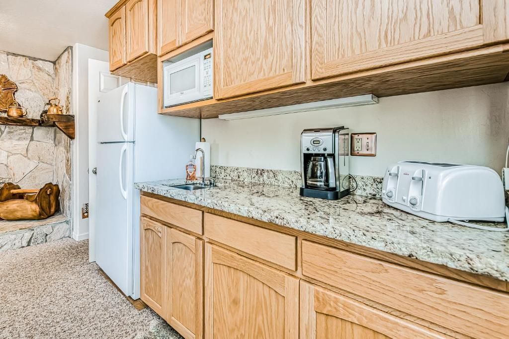 Bright kitchen with wood cabinets, white refrigerator, granite countertop, and appliances on the counter.